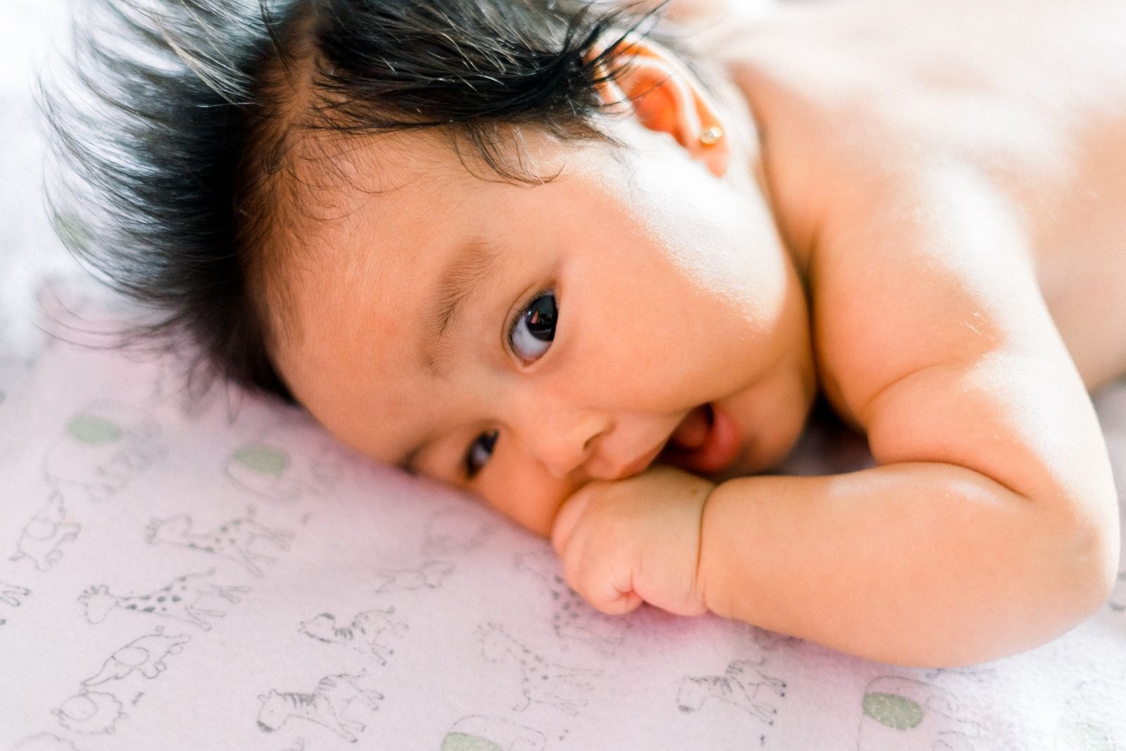 Baby liegt auf der Seite, das Ohr gut sichtbar, während es an der eigenen Hand kaut