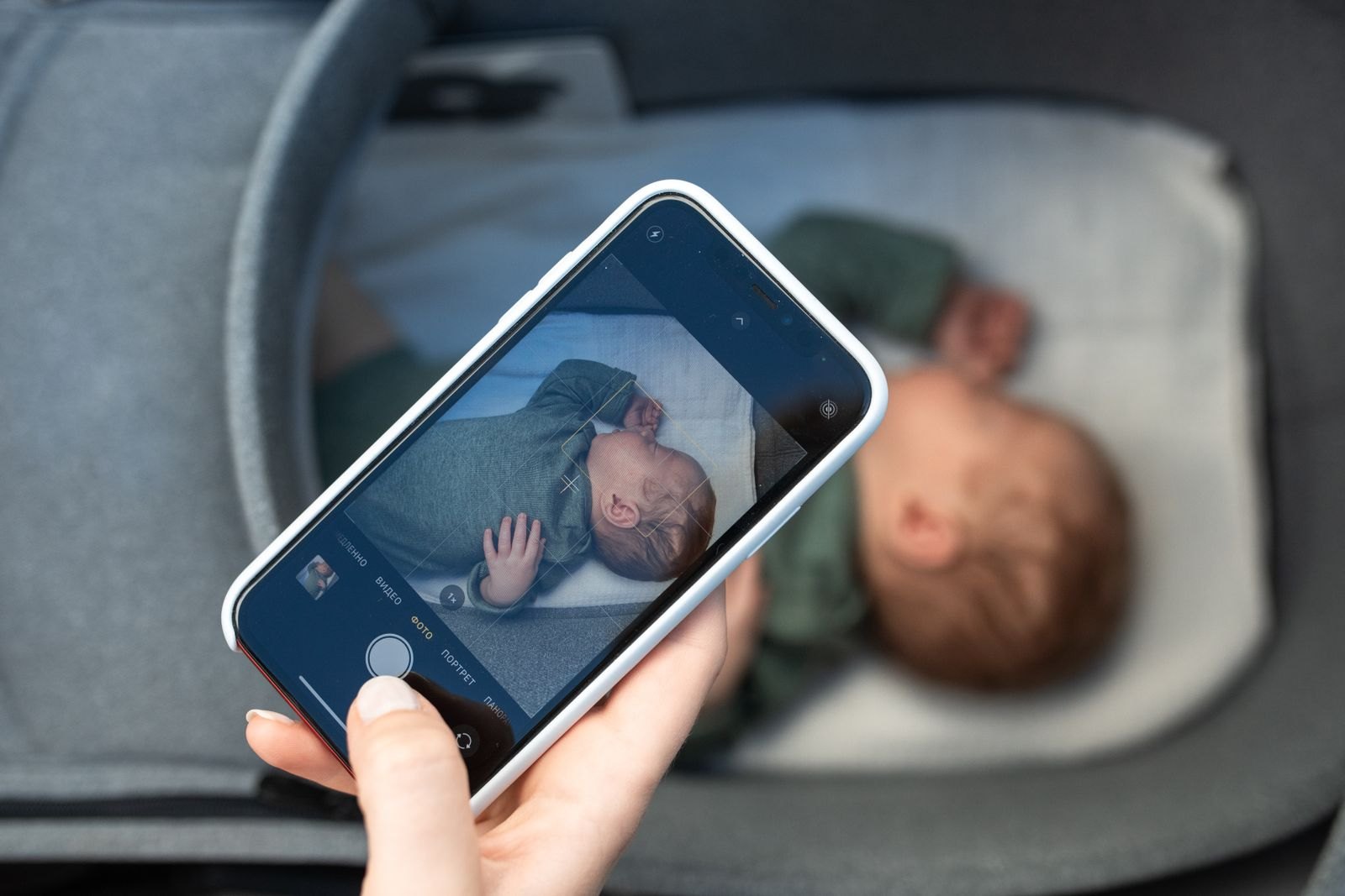 Elternteil hält ein Smartphone hoch, um ein schlafendes Baby aus der Nähe im Kamerabild zu prüfen