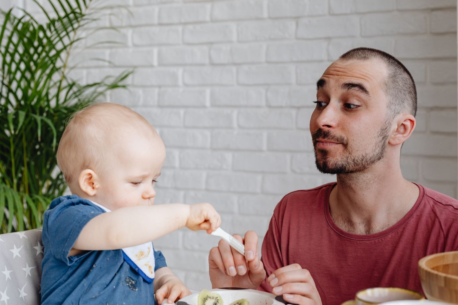 Baby im Hochstuhl greift selbst nach dem Löffel, den ein Elternteil hält