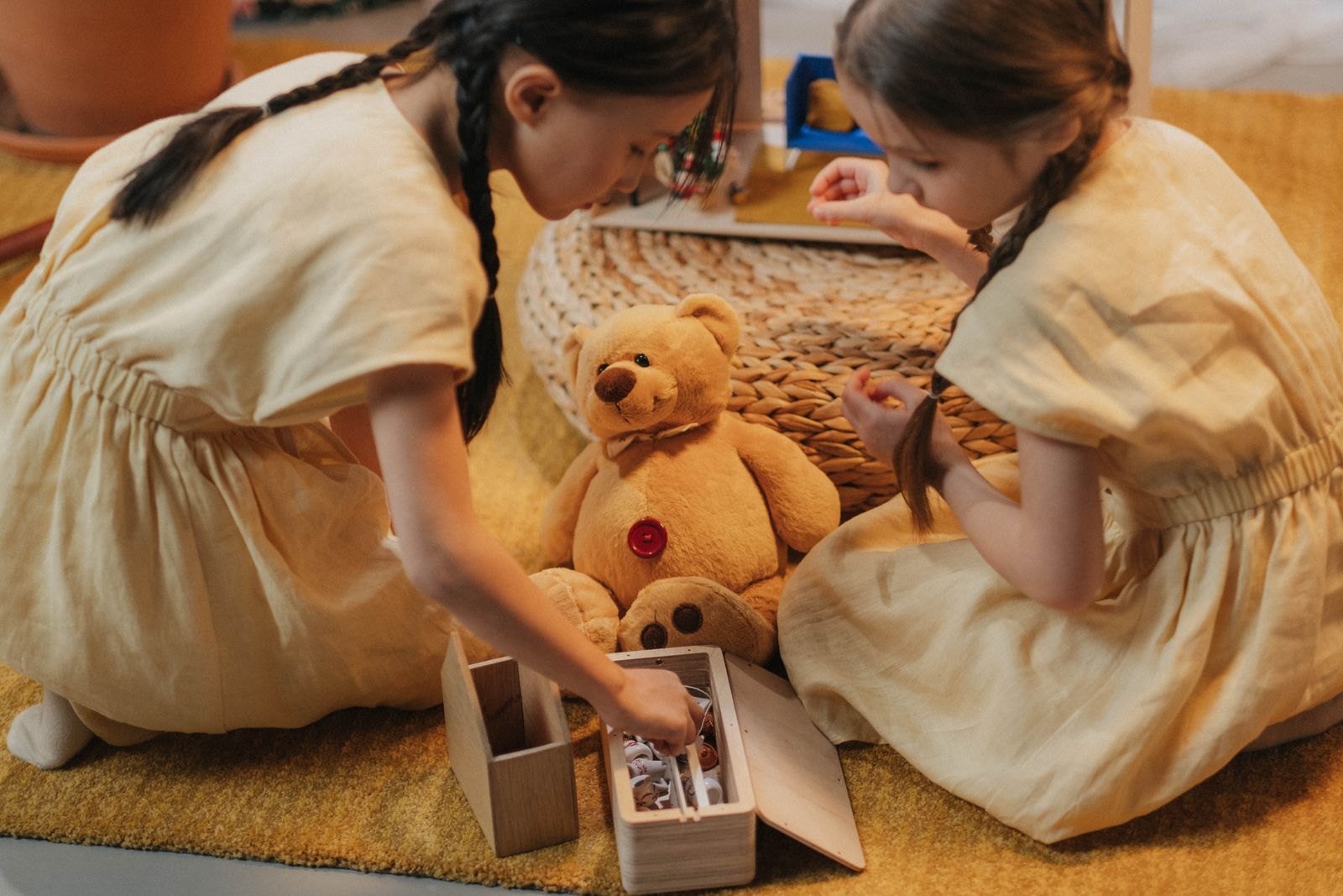 Zwei Kinder spielen zusammen auf dem Boden mit einem Stofftier und einer kleinen Kiste