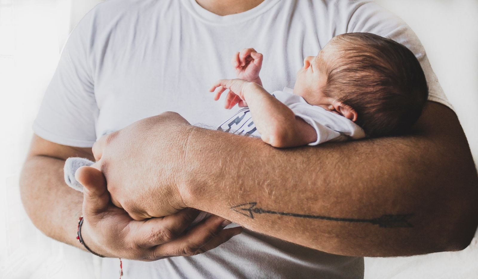 Vater hält sein Neugeborenes im Arm, ein Ärmchen ist reflexartig mit geöffneter Hand ausgestreckt
