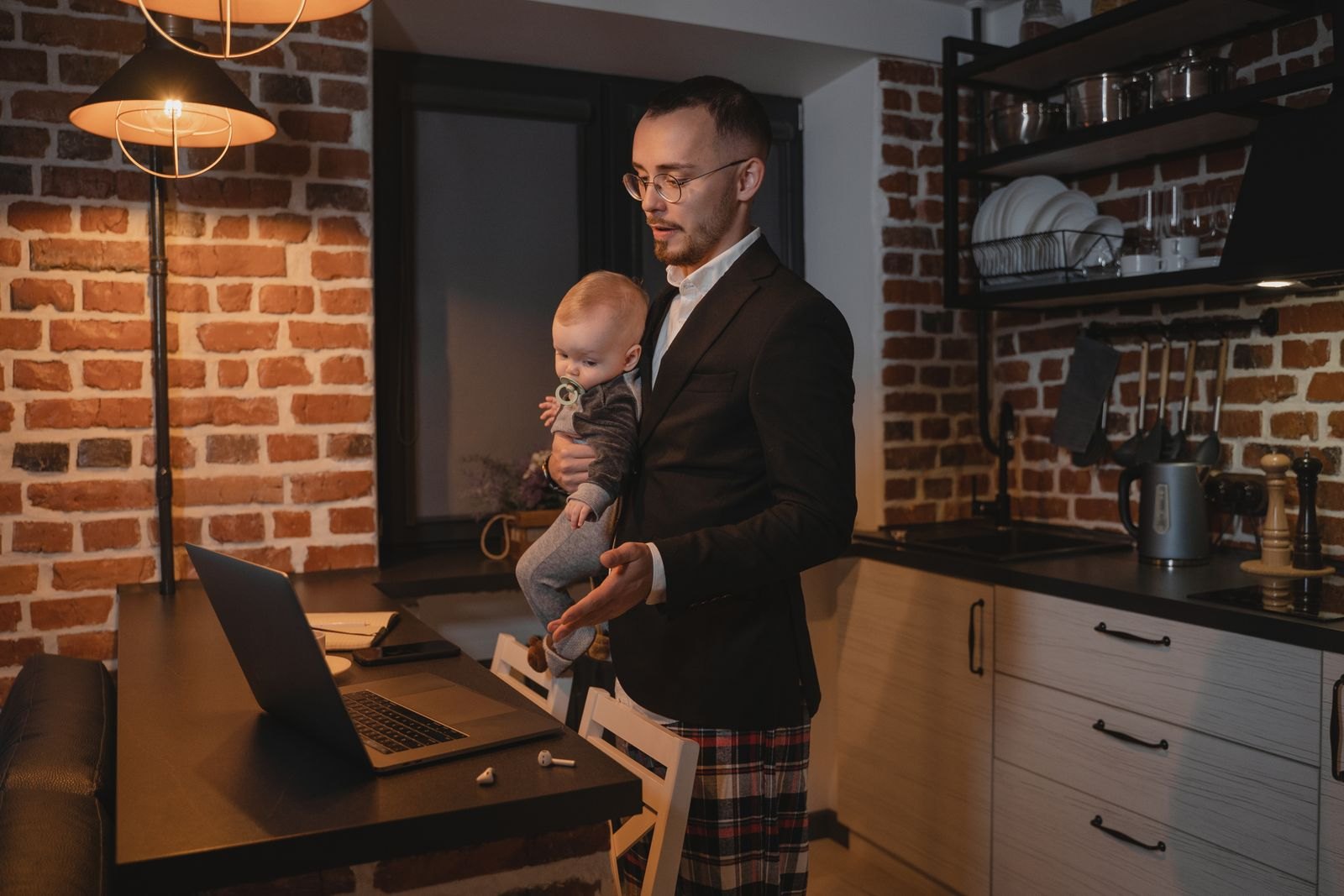 Vater hält abends spät das Baby, während er noch am Laptop arbeitet