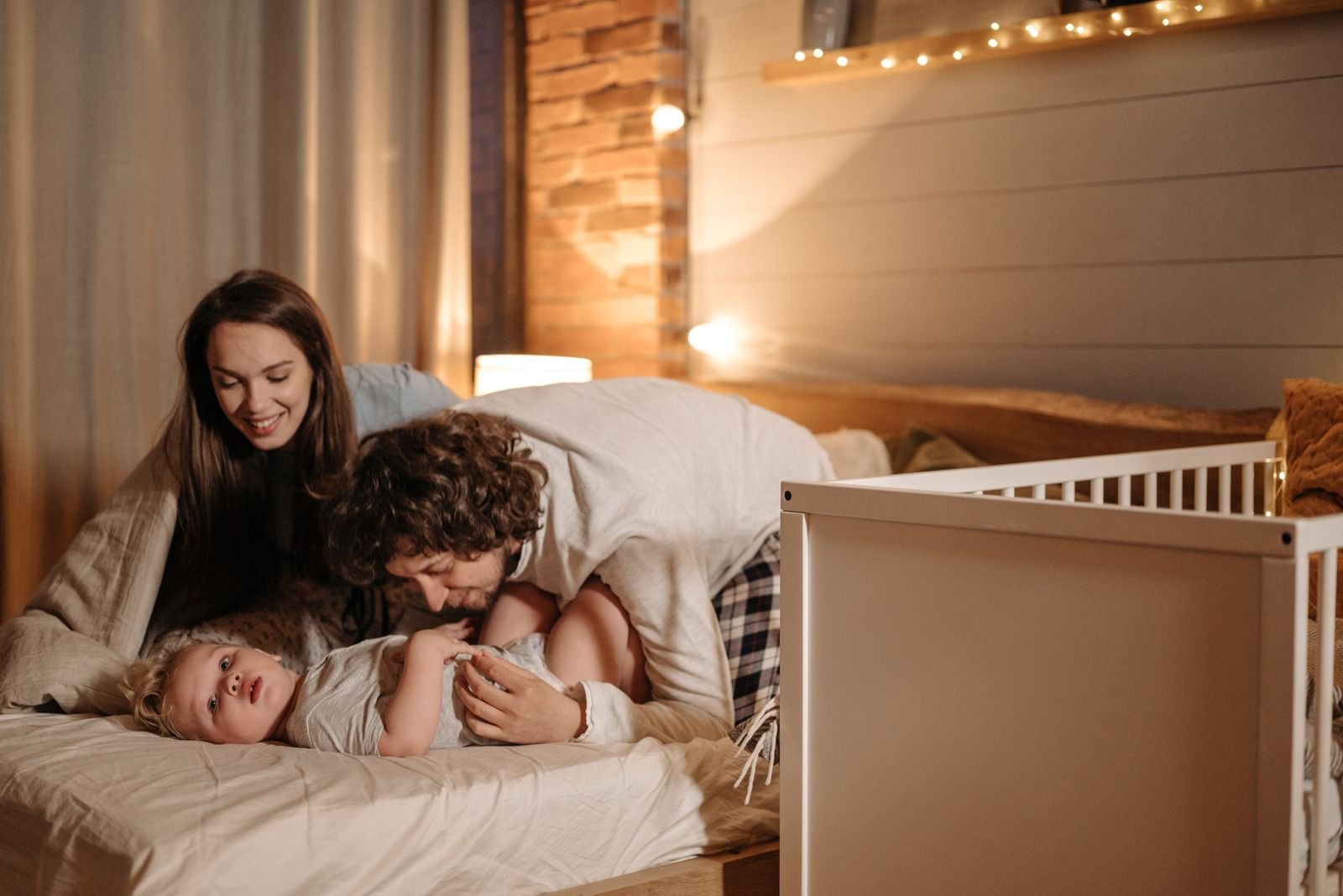 Eltern beruhigen abends im warmen Licht ihr Kind neben dem Gitterbett