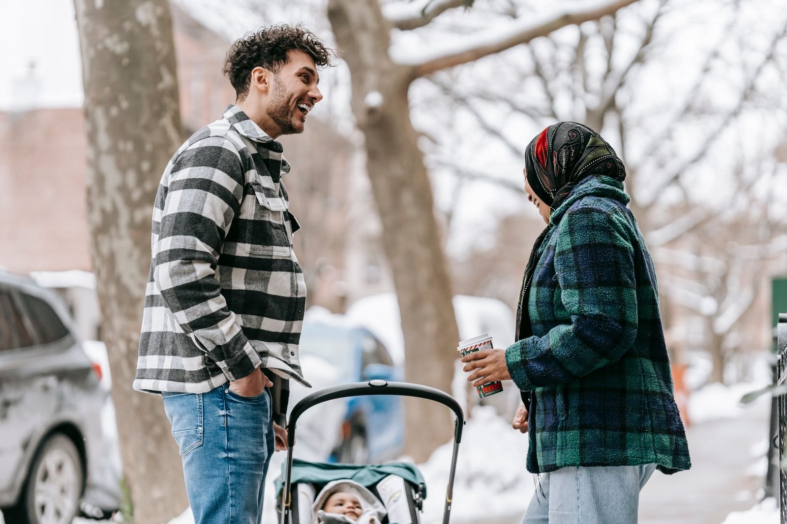 Zwei Elternteile unterhalten sich nebeneinander stehend neben einem Kinderwagen im Schnee