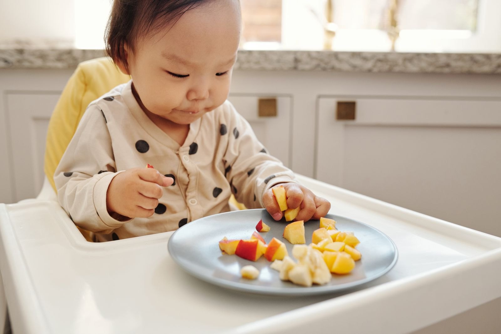 Baby isst selbstständig weiche, kleingeschnittene Obststücke mit den Fingern vom Teller
