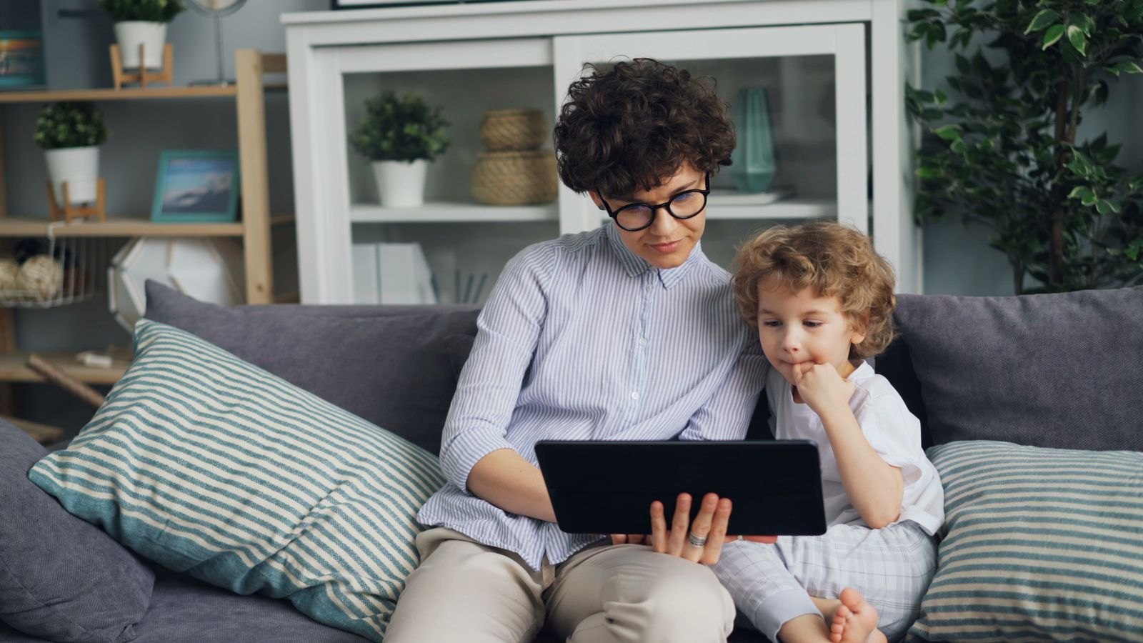 A parent and toddler watching a tablet together on the couch