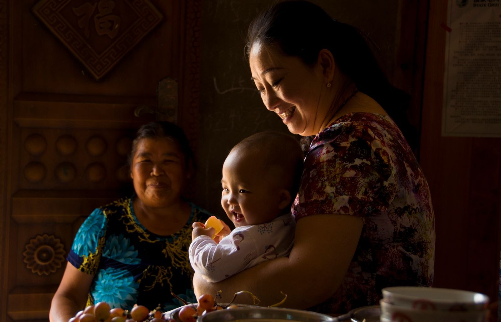 A grandmother holding a baby while the baby's mother looks on warmly