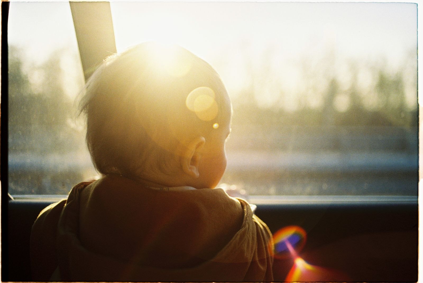 A toddler secured in a rear-facing convertible car seat in the back seat of a car