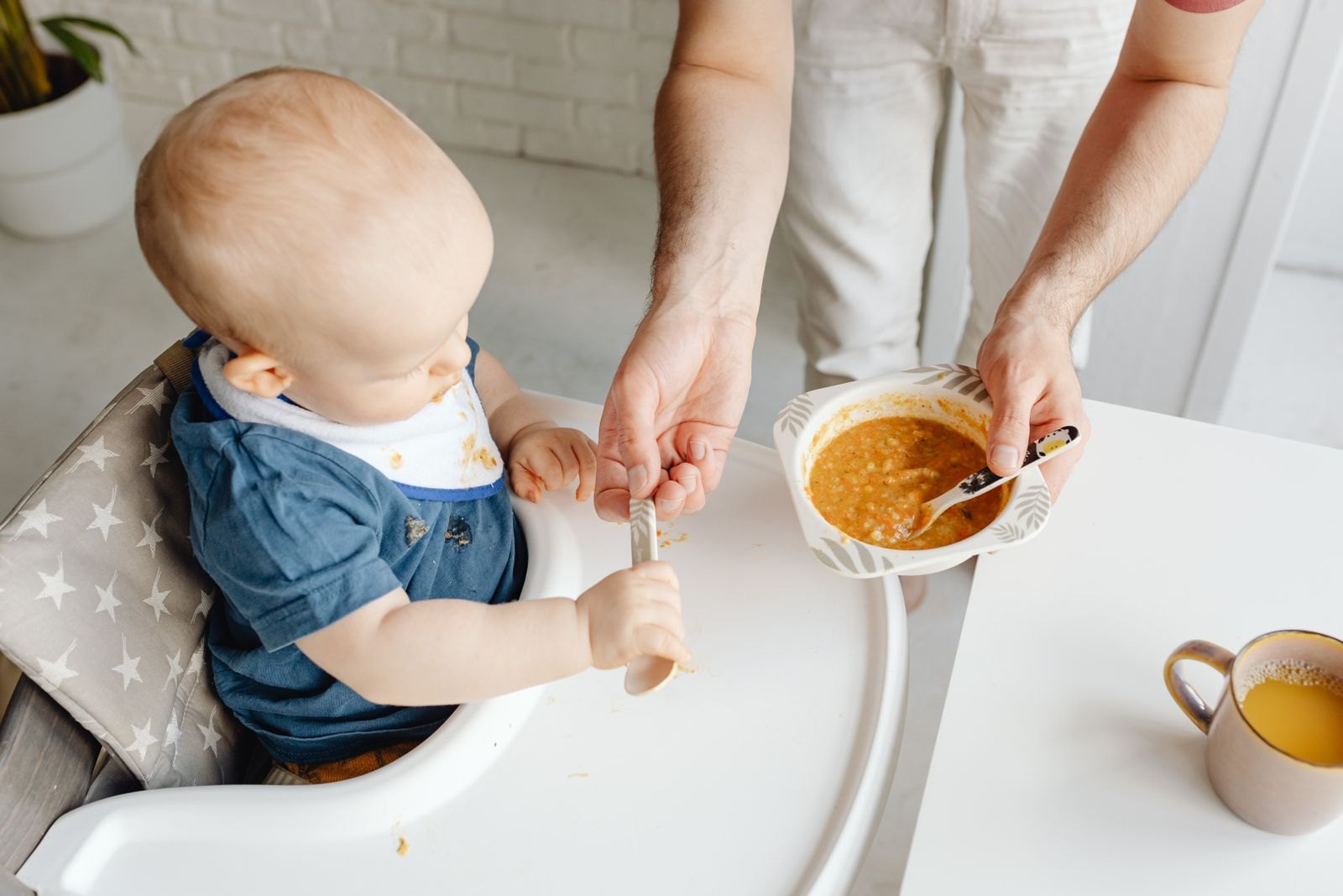A parent supervising a baby closely while the baby self-feeds at a high chair