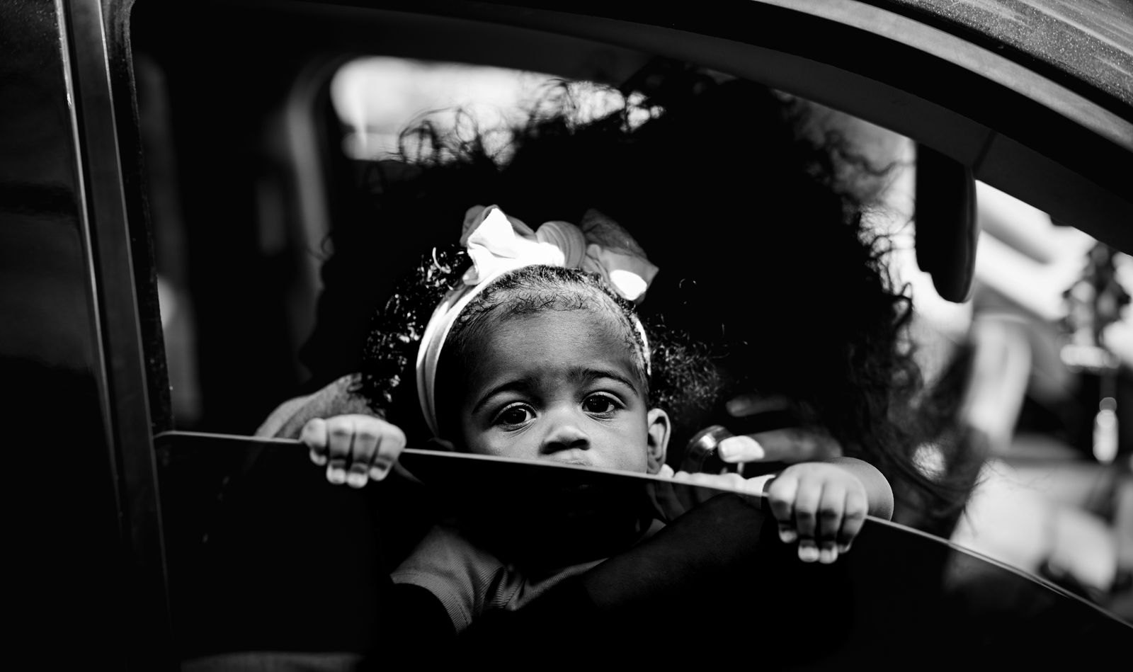 A toddler in the back seat of a car, looking out the window