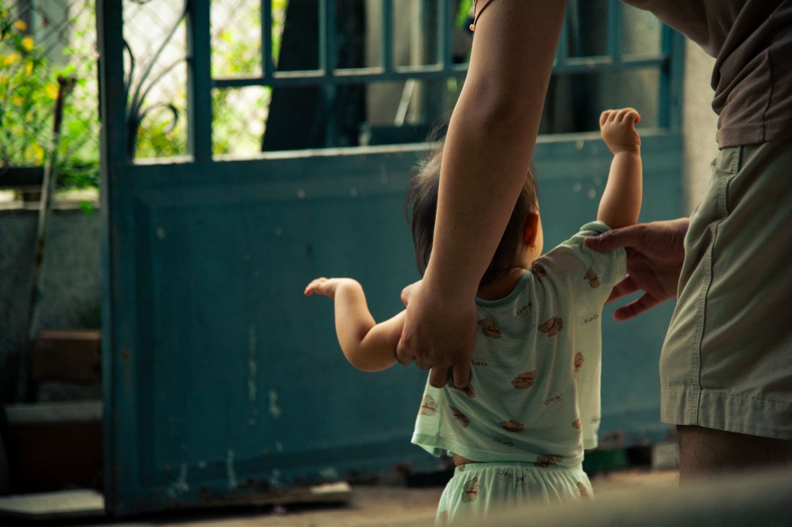 A toddler standing and taking assisted steps while holding a parent's hand