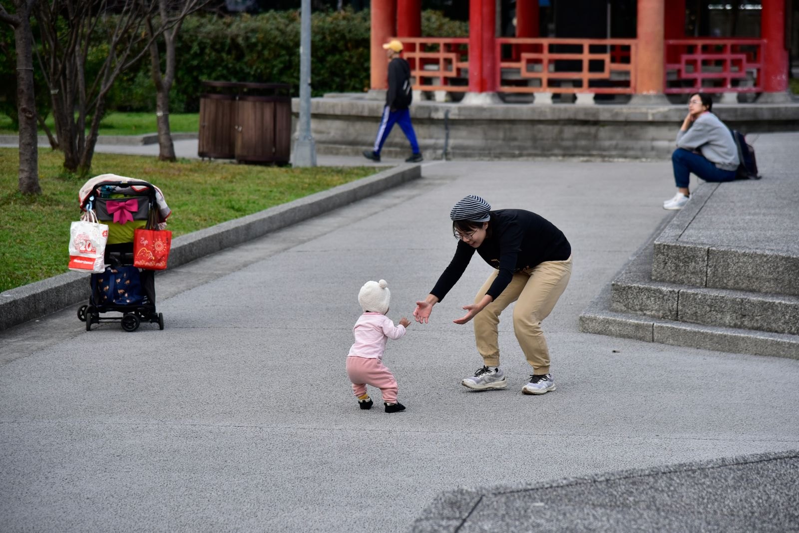 A toddler walking outdoors near a stroller during a family outing