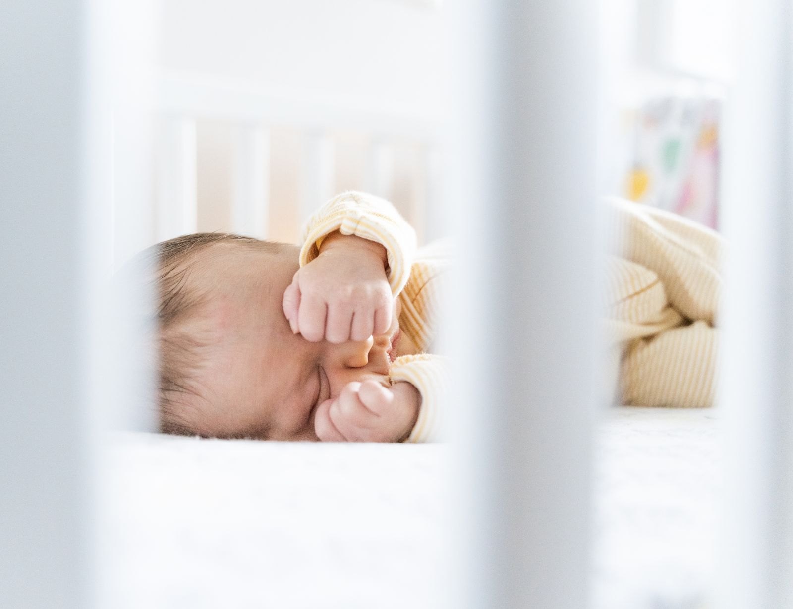 An infant sleeping on their back in a bare crib with only a fitted sheet
