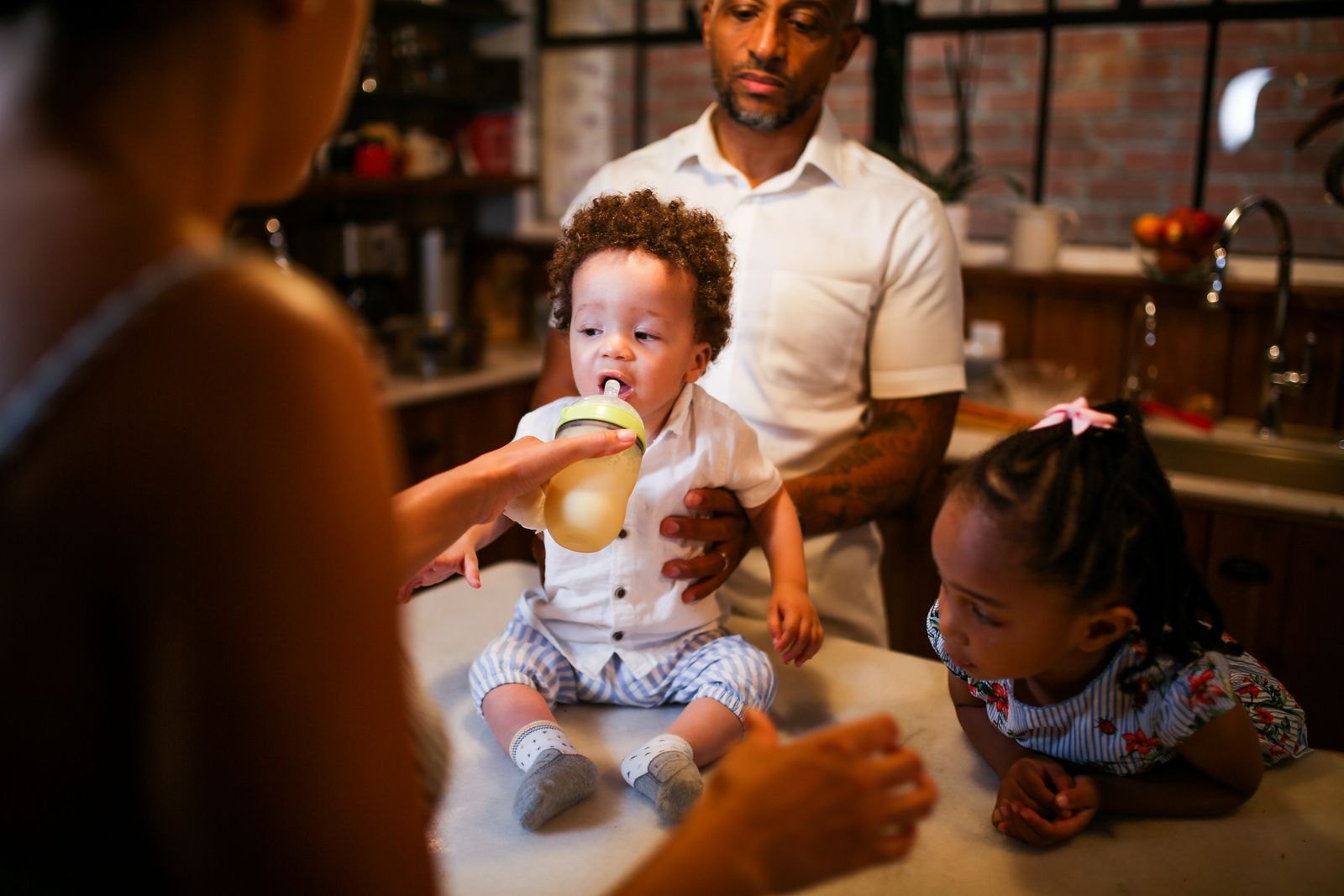 A father holding a toddler while another parent feeds the child and an older sibling looks on