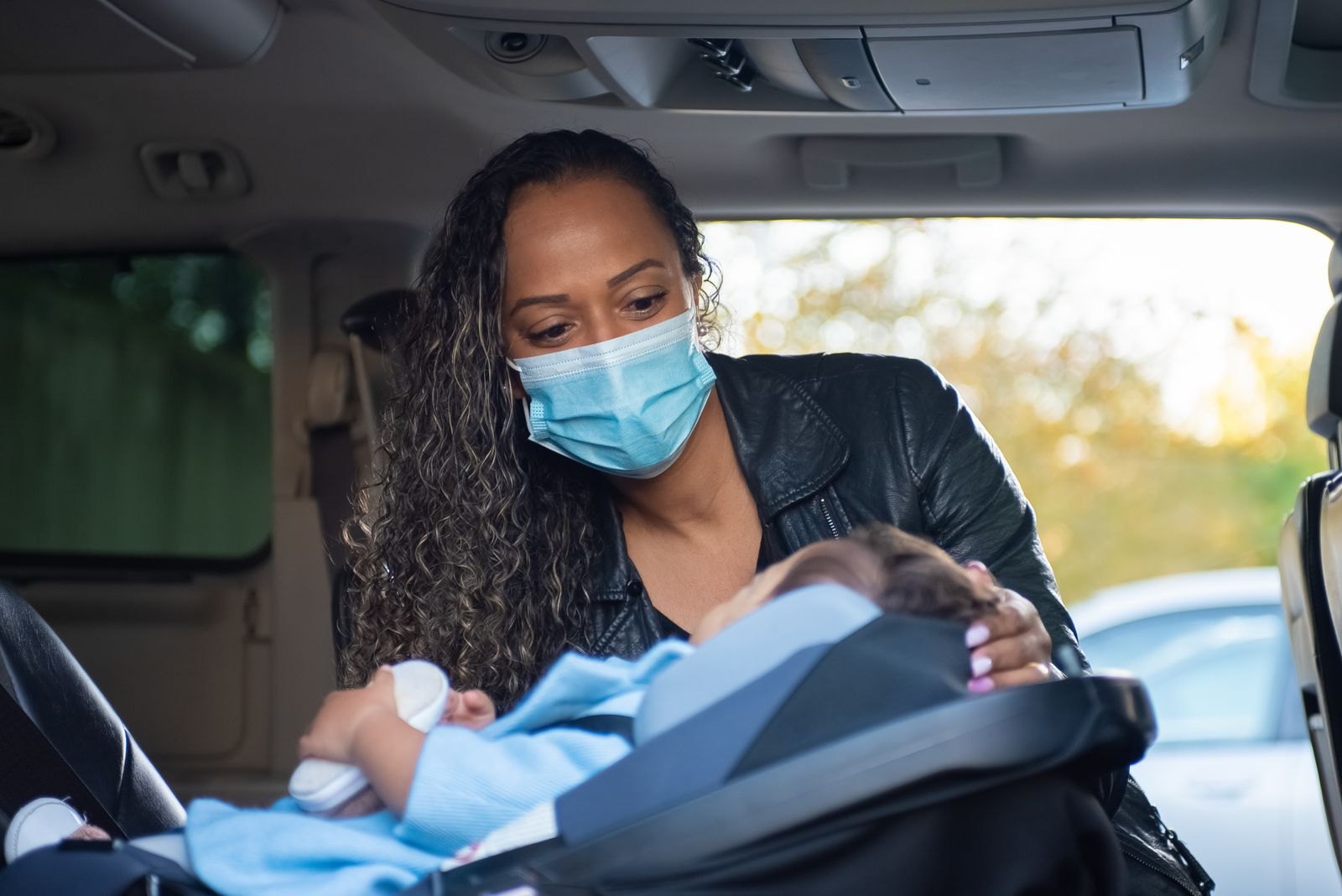 A parent securing a baby into a car seat inside a car