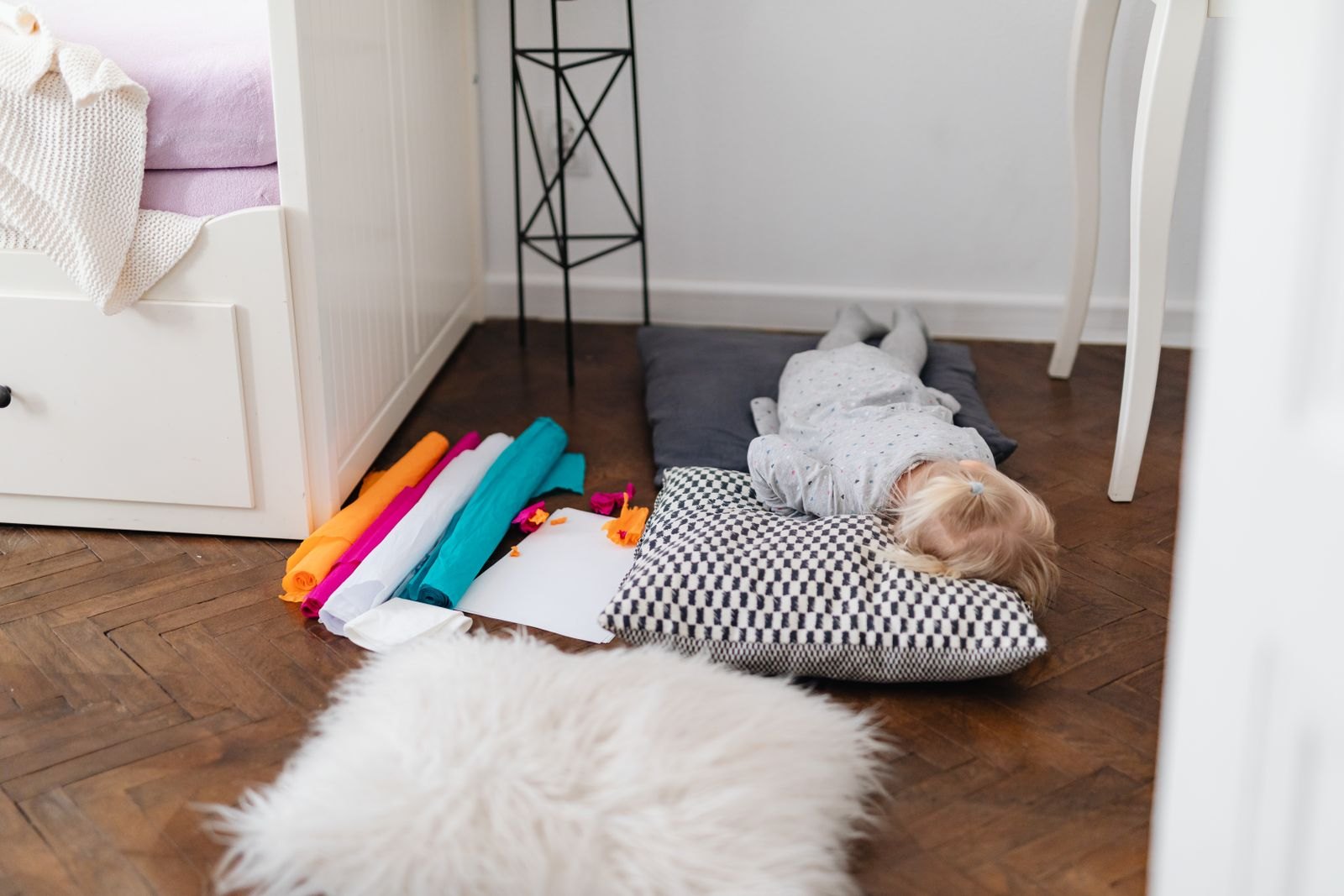 A toddler lying face-down on a floor pillow amid scattered craft supplies during a meltdown