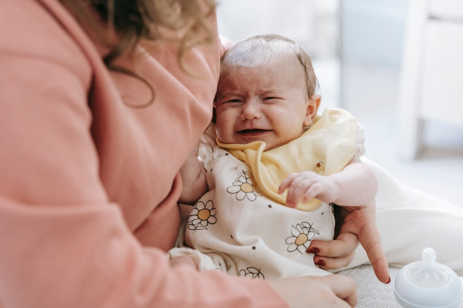 Un bebé llorando mientras su madre lo consuela cerca del cuerpo