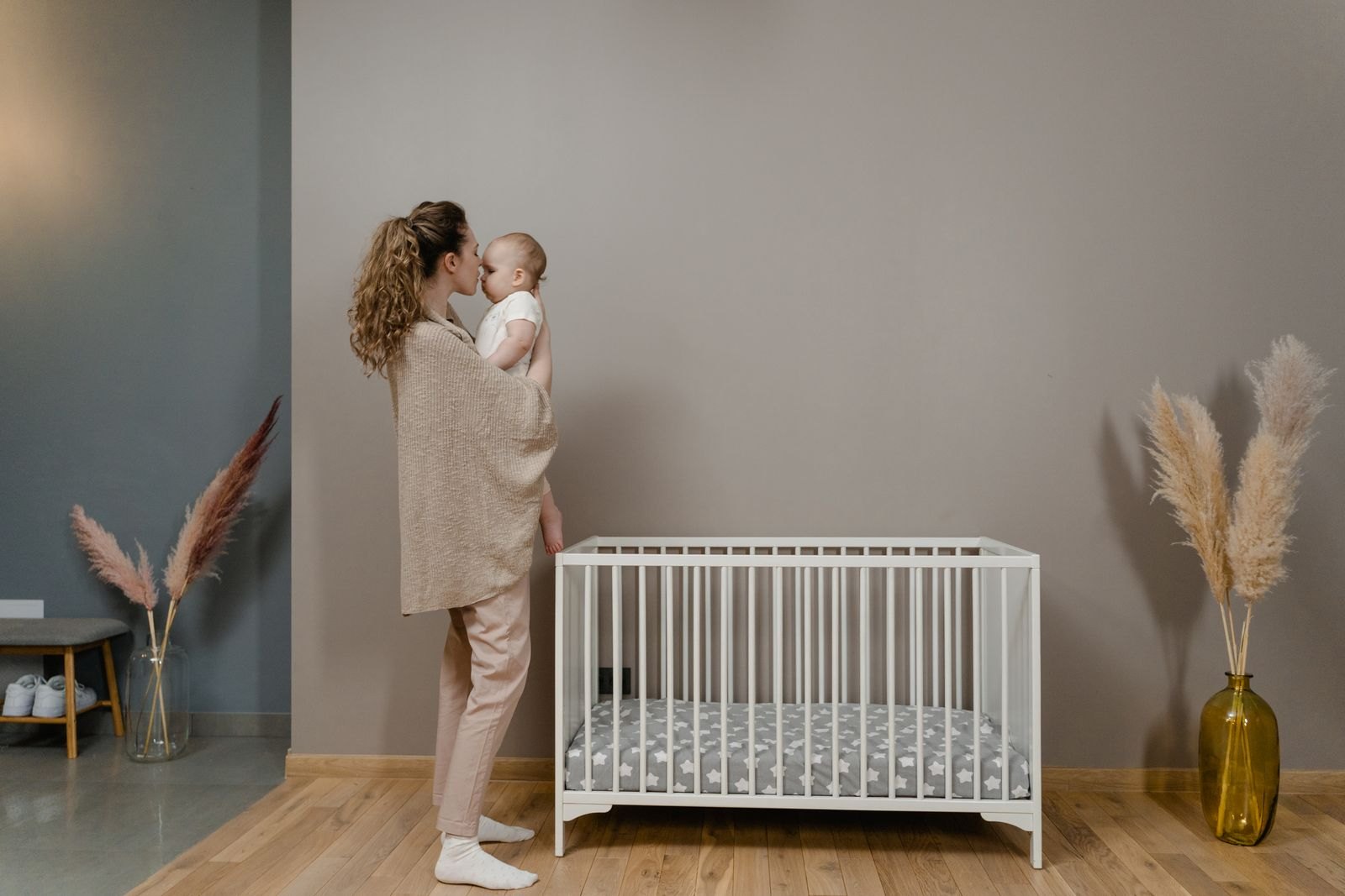 Una madre con su bebé junto a una cuna con superficie firme y plana, la configuración de sueño seguro recomendada