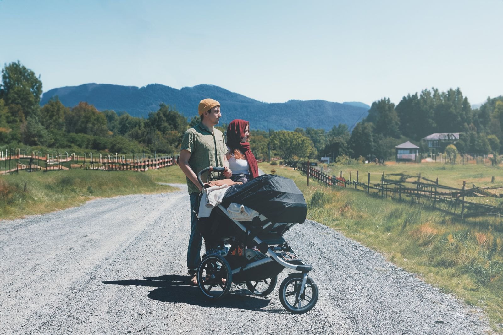 Una familia paseando con un cochecito tipo jogger por un camino de grava con montañas al fondo