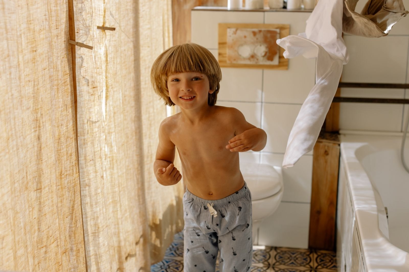 Un niño sonríe y se aleja corriendo sin camiseta mientras esta vuela por el aire en el baño