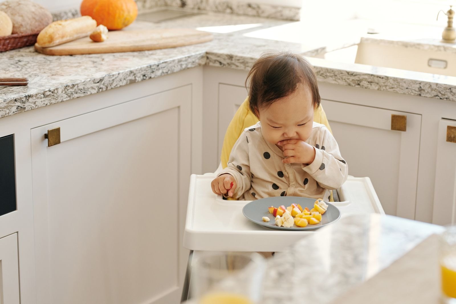 Bebé comiendo trozos de fruta y pan con la mano sentado en la trona