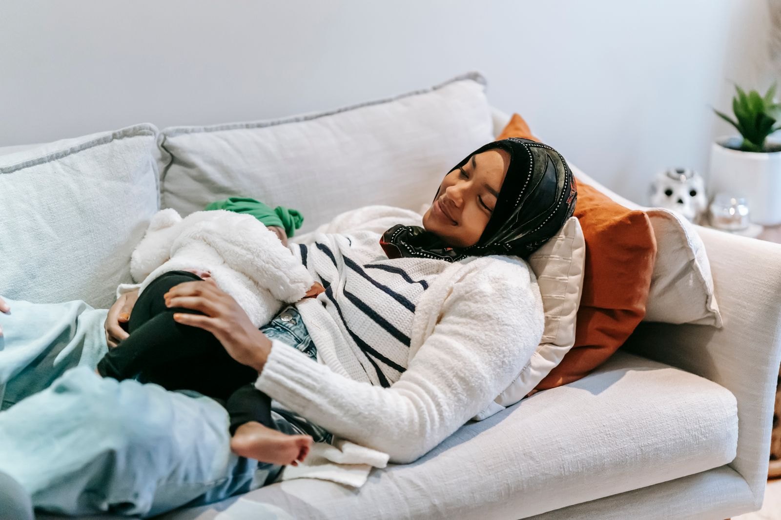 Una madre descansa en el sofá con su bebé en brazos durante una toma nocturna, en un ambiente tranquilo y con poca luz