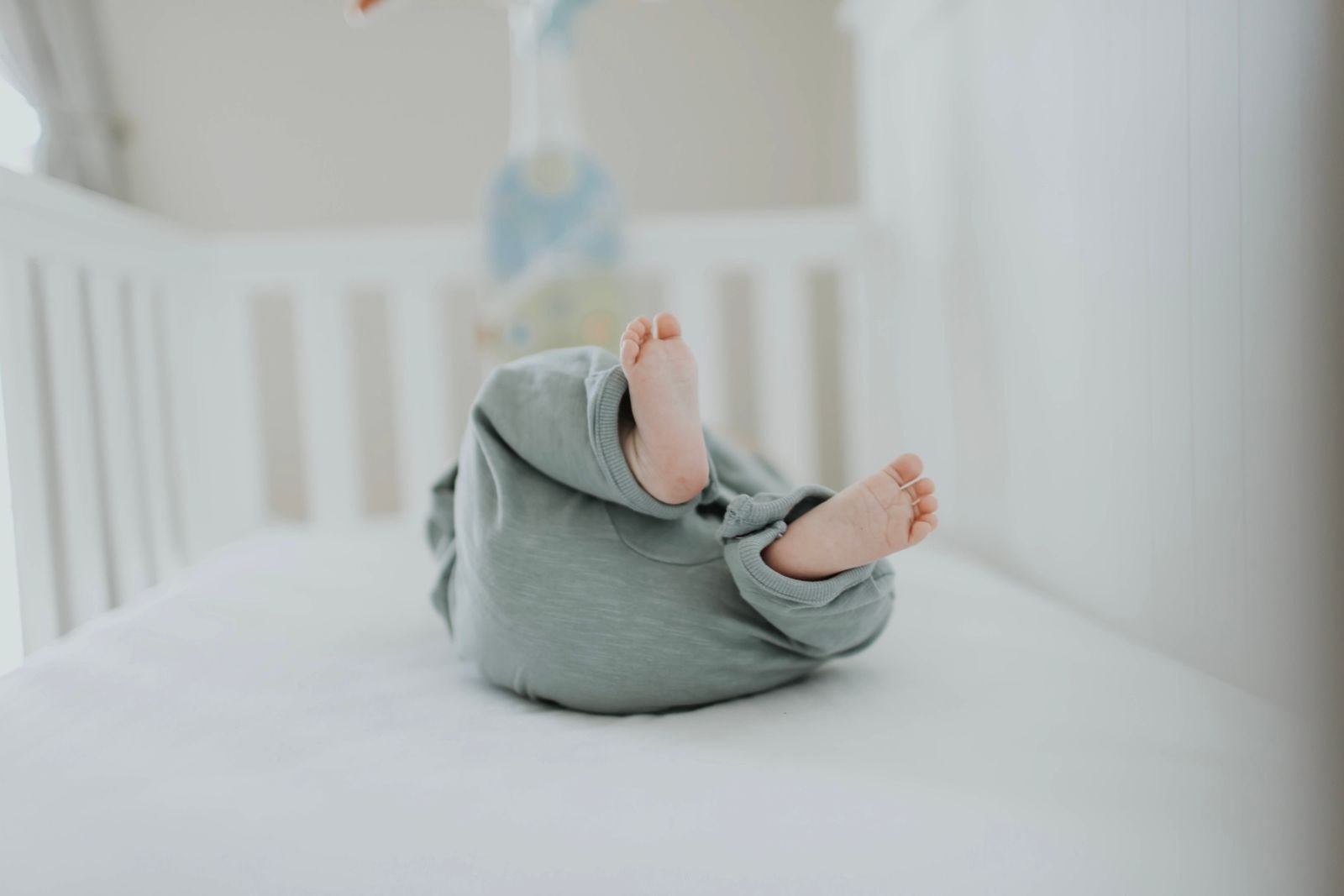 Pieds de bébé dépassant d'une gigoteuse dans un lit à barreaux, mobile suspendu en arrière-plan