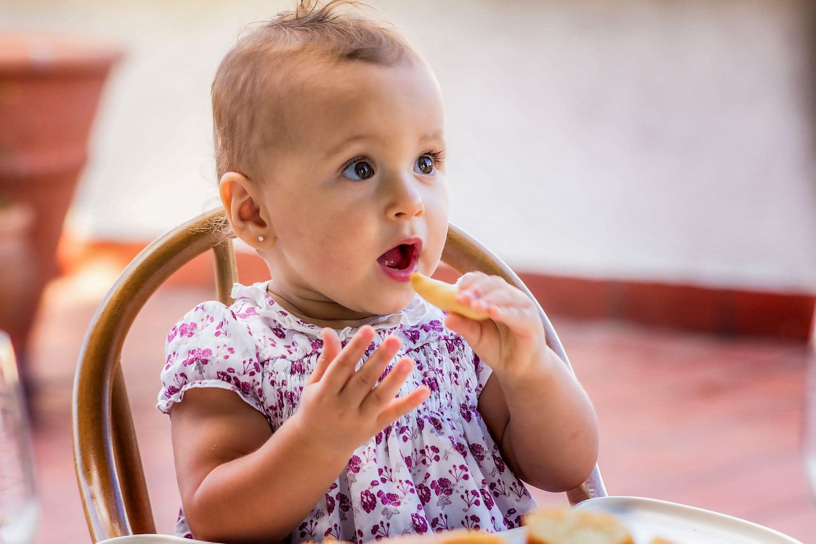 Un bébé assis dans une chaise haute portant lui-même un morceau de nourriture à sa bouche