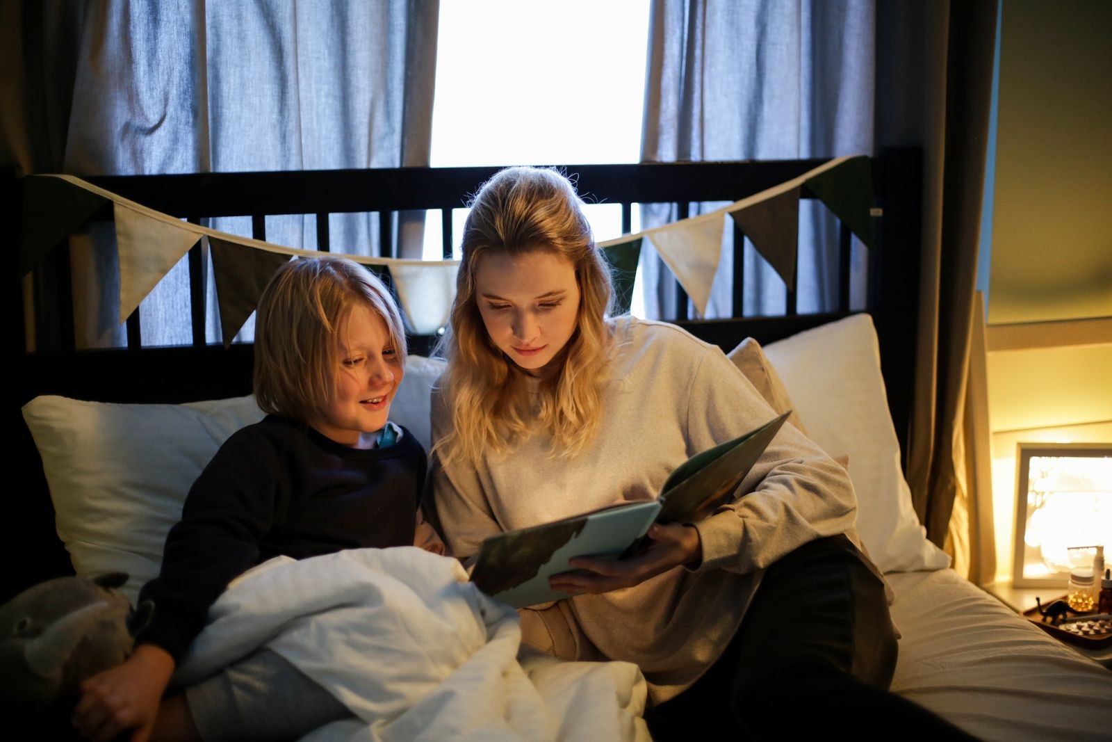 Une mère lit une histoire du soir à son enfant dans une chambre faiblement éclairée par une lampe de chevet