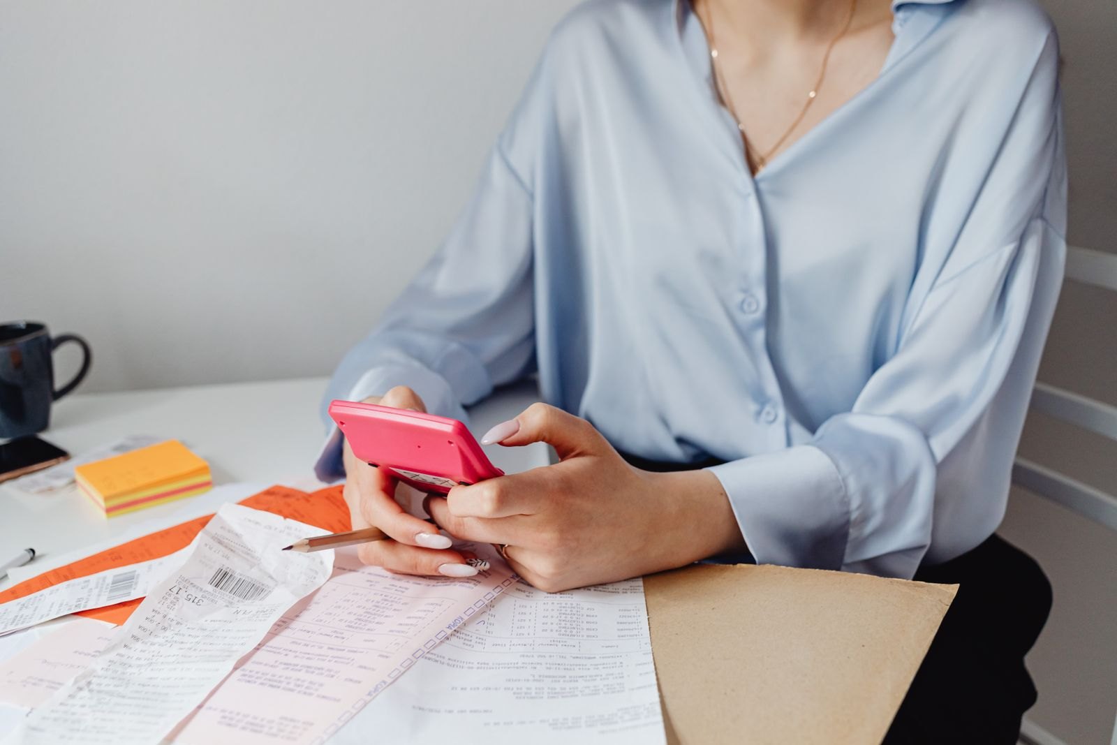 Une personne consulte des tickets de caisse et une calculatrice sur un bureau pour faire ses comptes