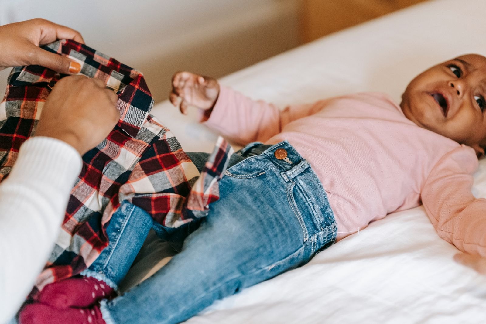 Un parent essaie d'habiller un bébé allongé qui tend le bras et proteste
