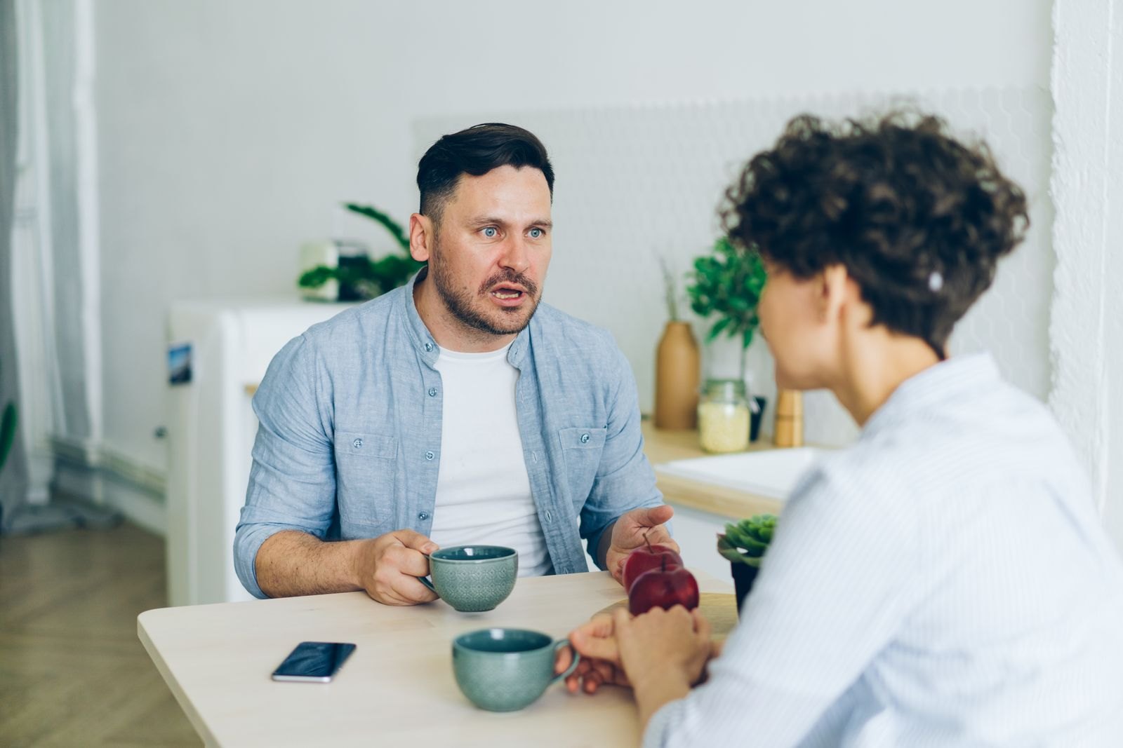Un couple assis à la table de la cuisine, mains posées l'une sur l'autre, en pleine conversation sérieuse autour d'un café