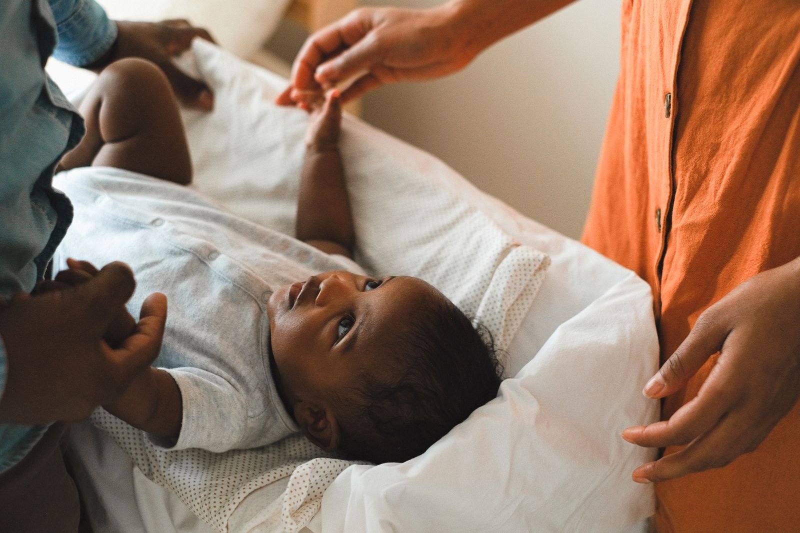 Un nouveau-né allongé, entouré par ses deux parents qui l'observent avec attention