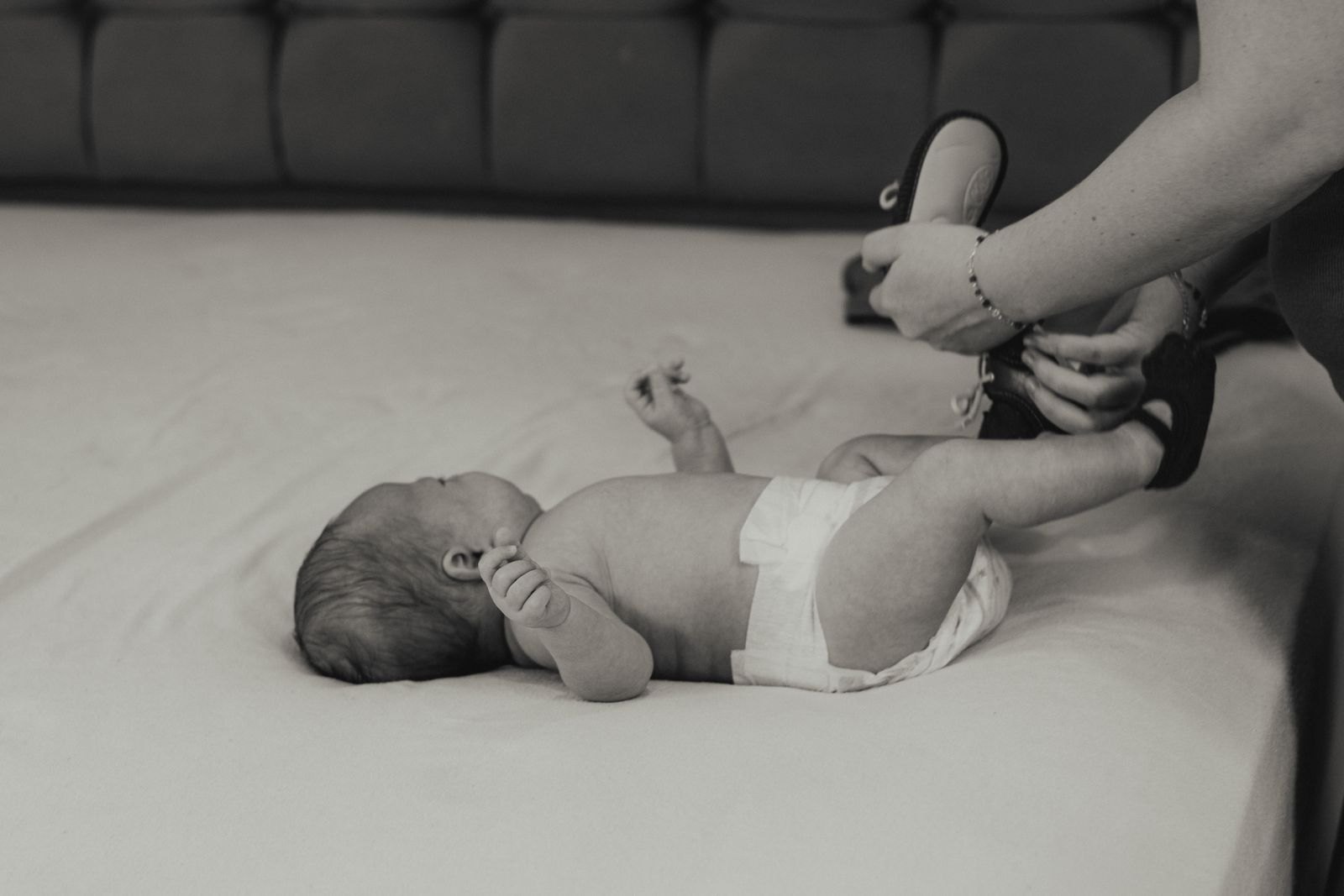 Nouveau-né allongé sur le dos, un bras étendu et la main ouverte, pendant qu'un parent lui tient doucement la jambe