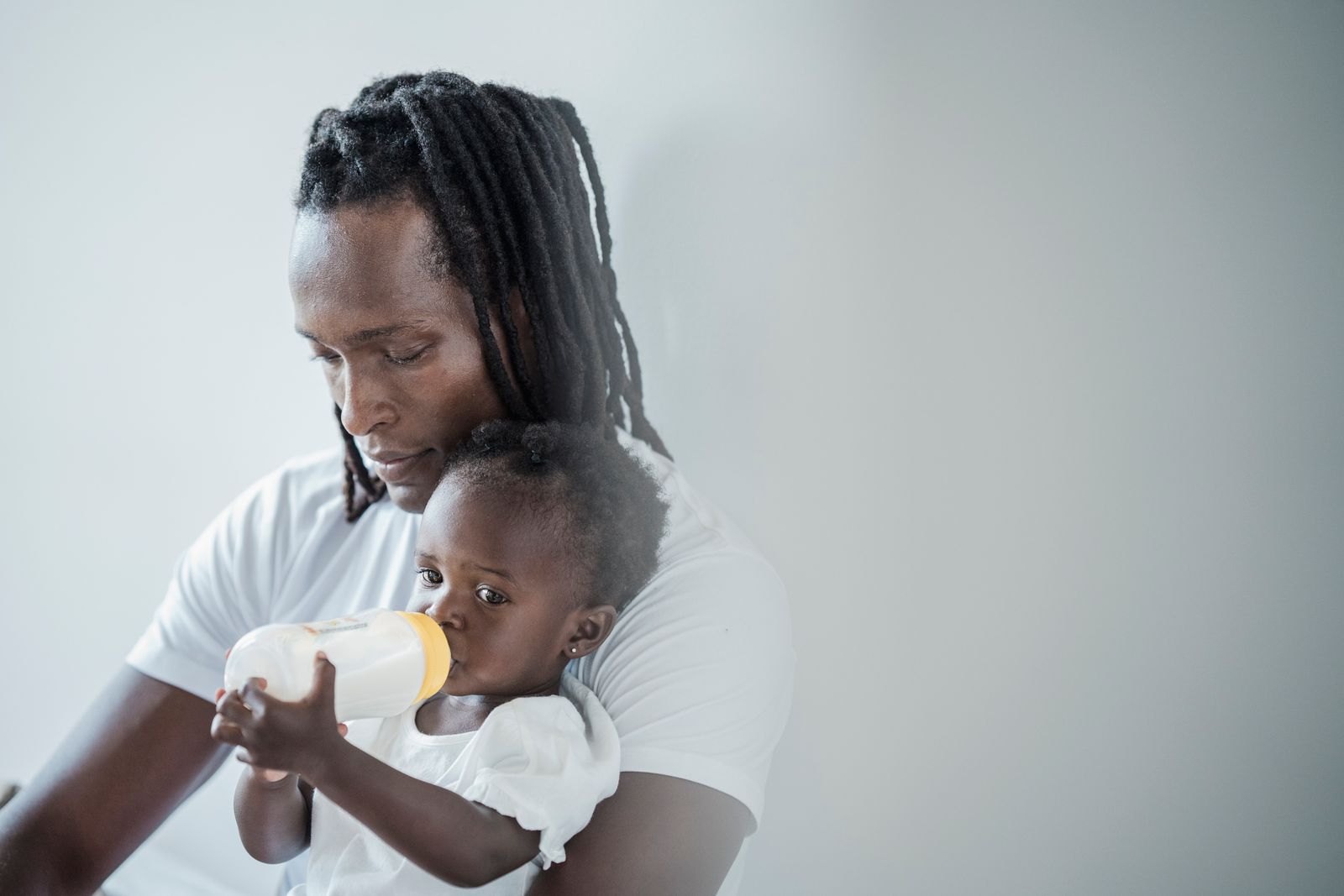 Un père donne le biberon à son bébé, tenu bien droit et proche de lui