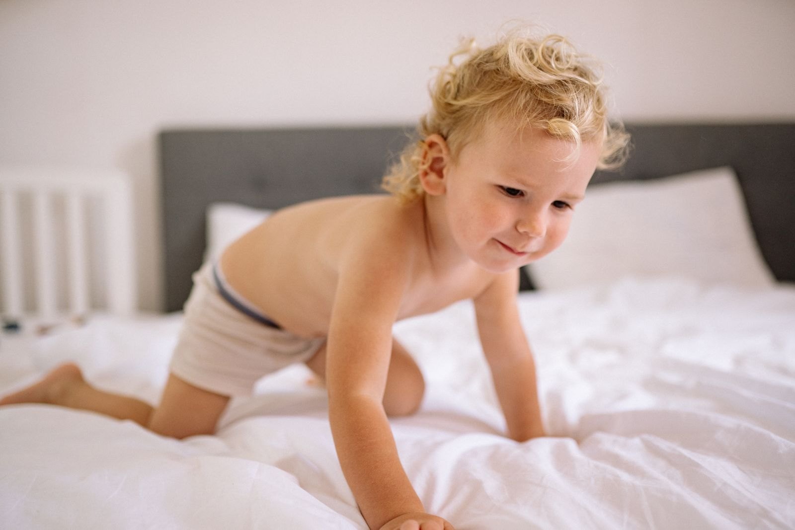 Un tout-petit à quatre pattes sur un lit en pleine journée, éveillé et joueur, sans aucun signe de fatigue