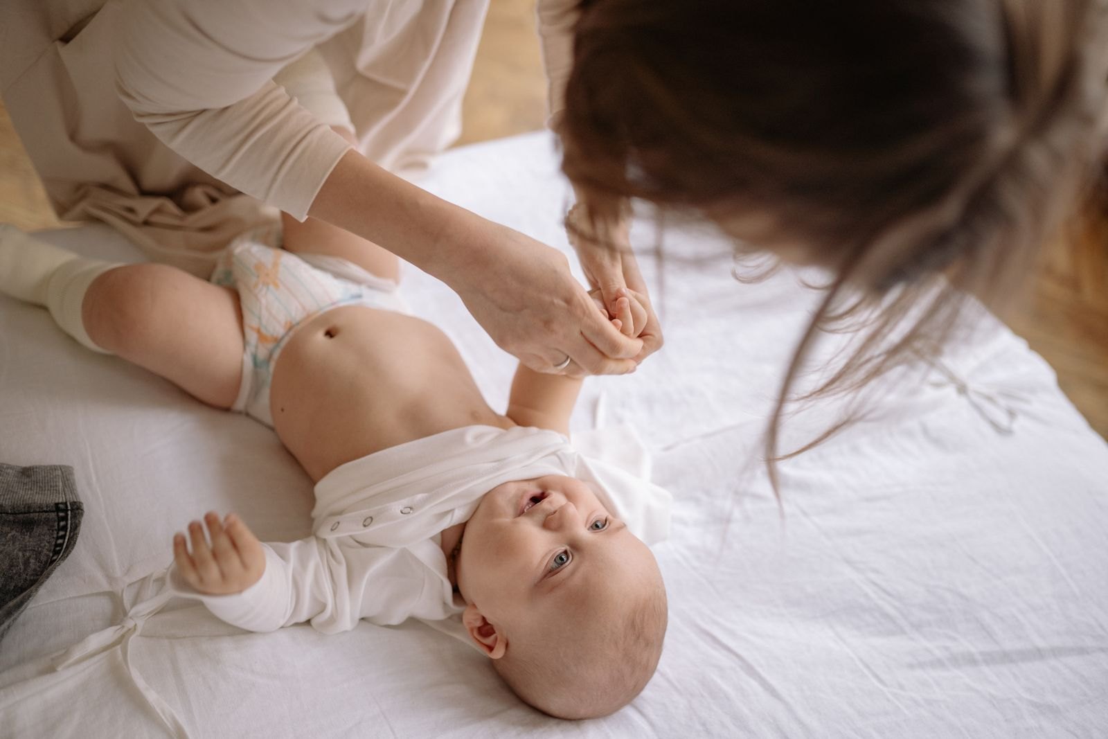 Un parent change la couche de son bébé sur un lit, dans une pièce lumineuse
