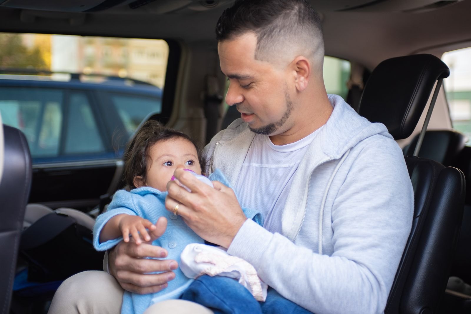 Un parent installe un bébé à l'arrière d'une voiture, siège auto visible à côté