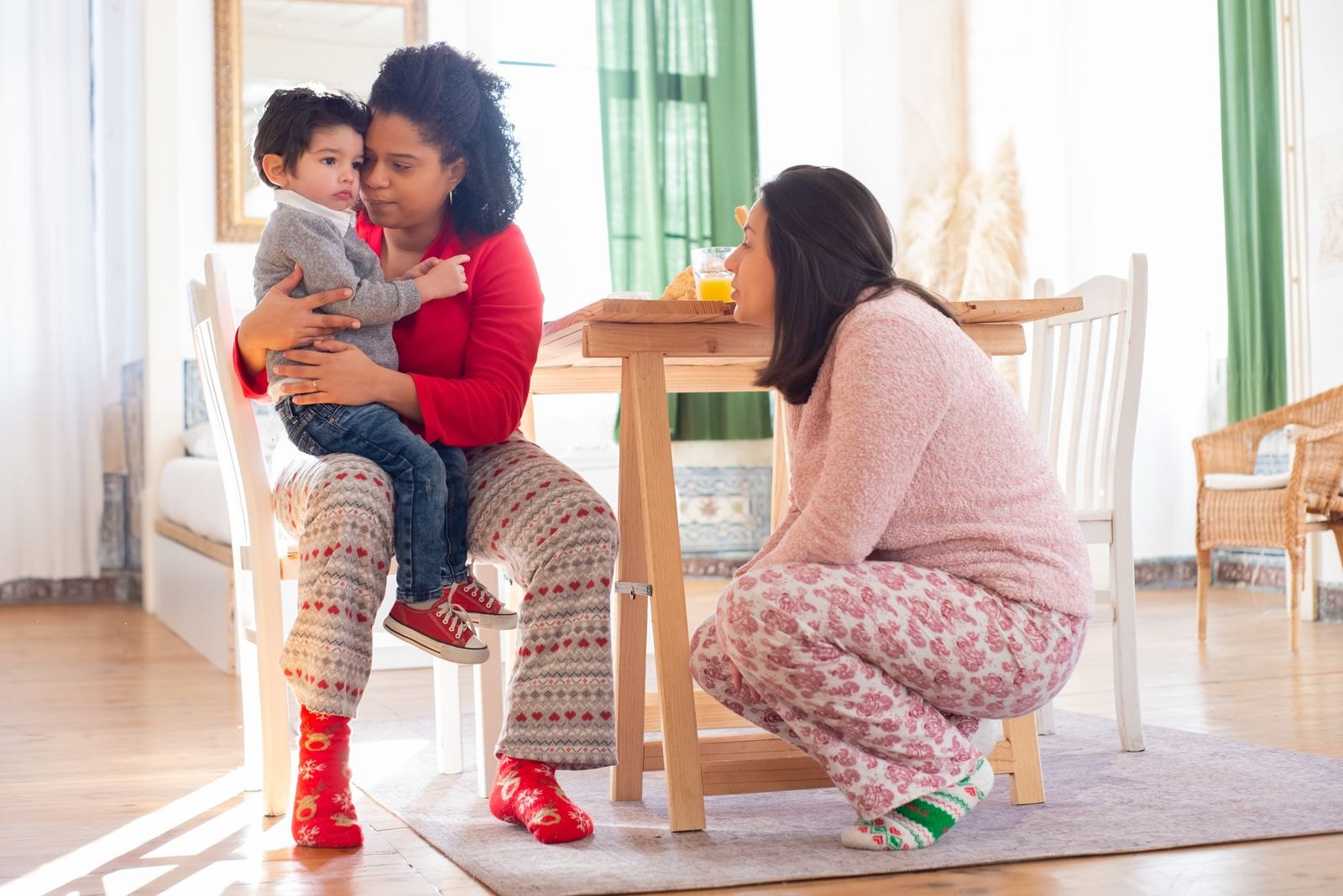 Una madre tiene in braccio un bambino piccolo dall'aria contrariata mentre un'altra persona gli parla con calma all'altezza degli occhi
