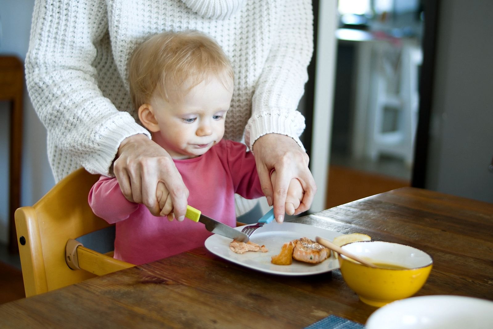 Un genitore taglia con cura il cibo in pezzi piccoli e sicuri per un bambino seduto al seggiolone