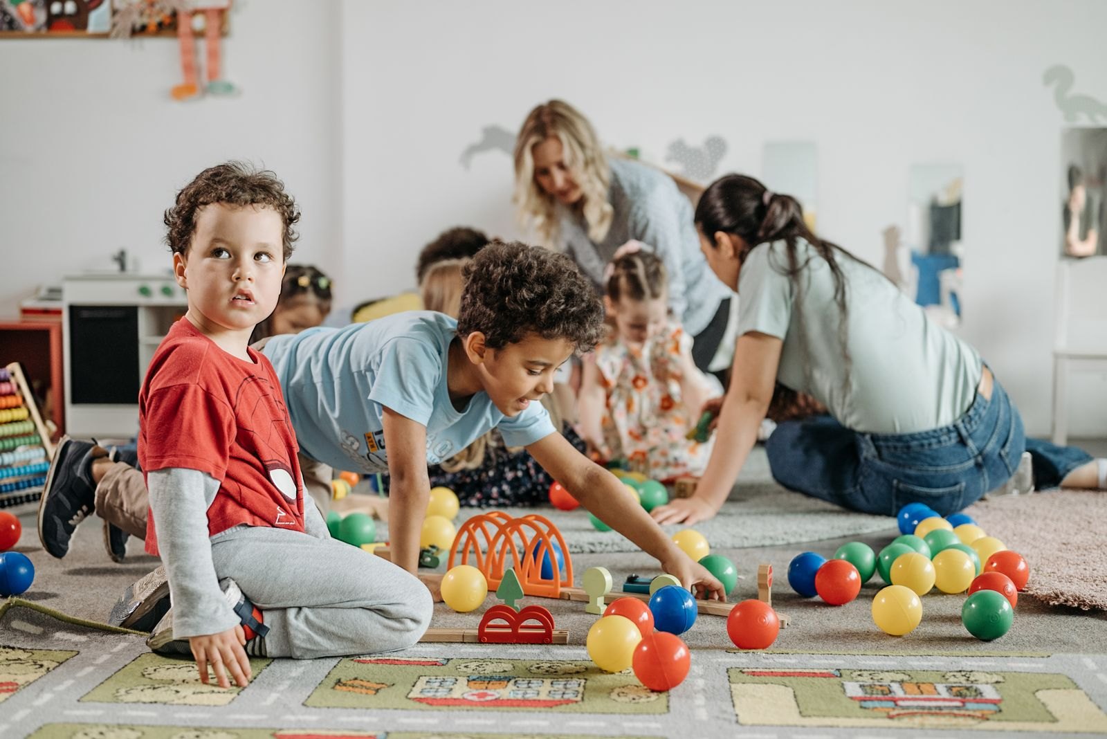 Un gruppo di bambini piccoli gioca a terra al nido con educatrici presenti