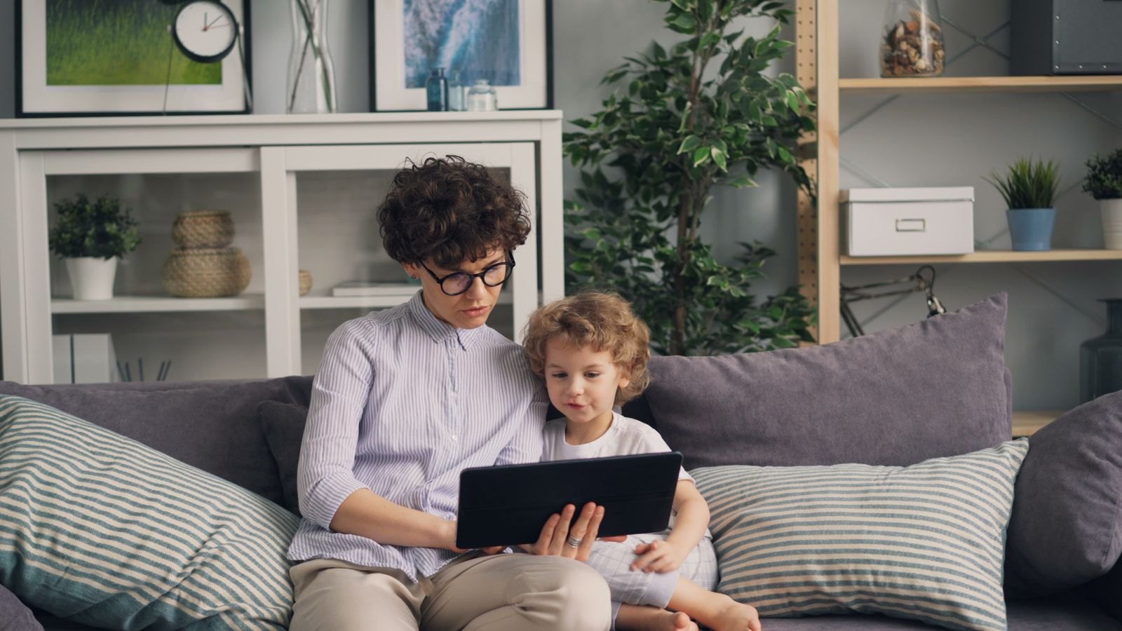 Un genitore guarda un tablet insieme a un bambino piccolo seduti sul divano