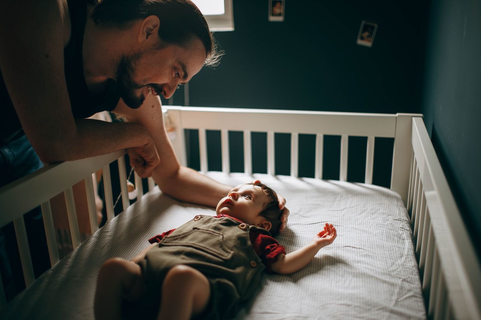 Un padre si china sorridente sulla culla per accudire il bambino in una stanza in penombra