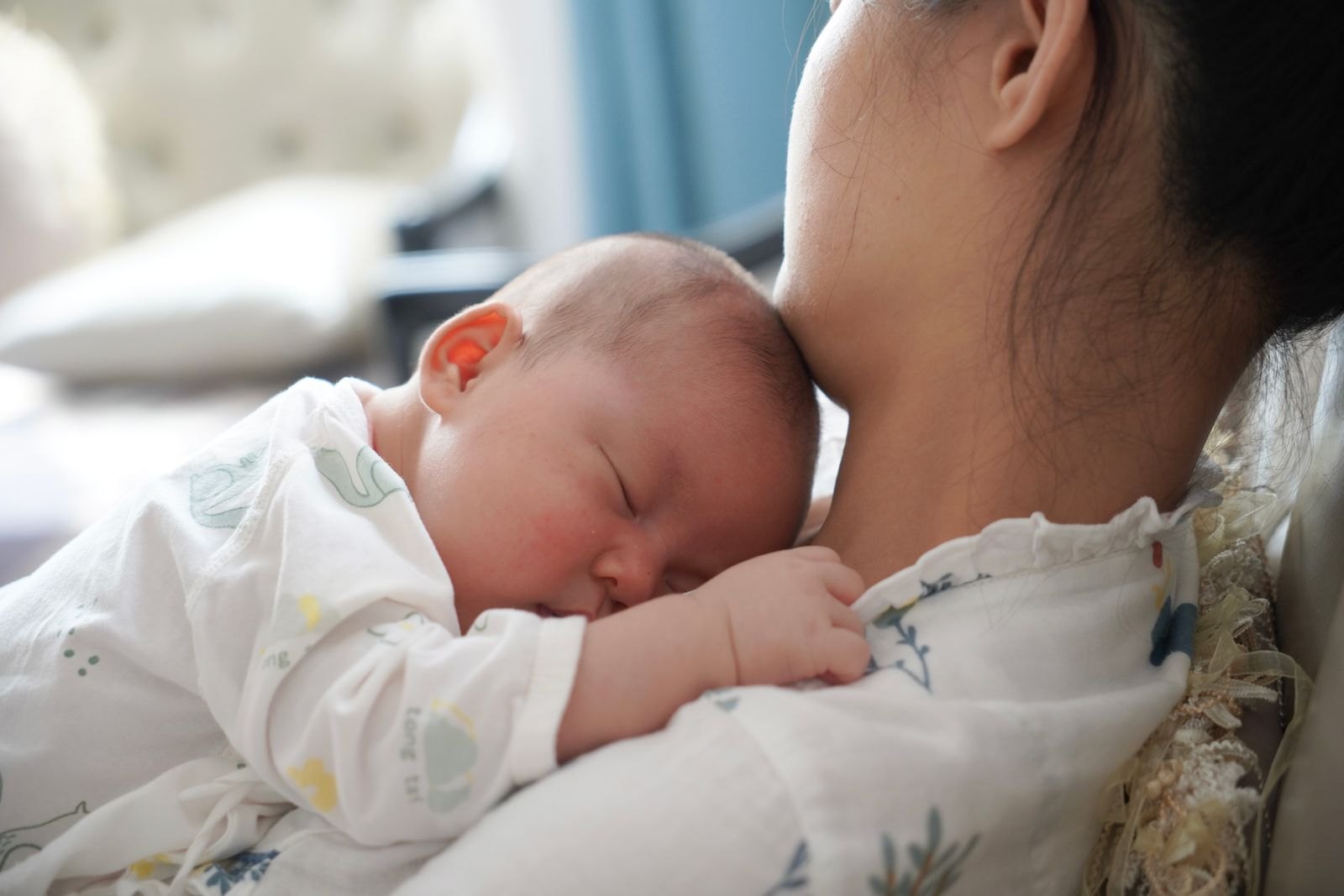 親の肩にもたれて眠る新生児、授乳後にげっぷをさせている様子