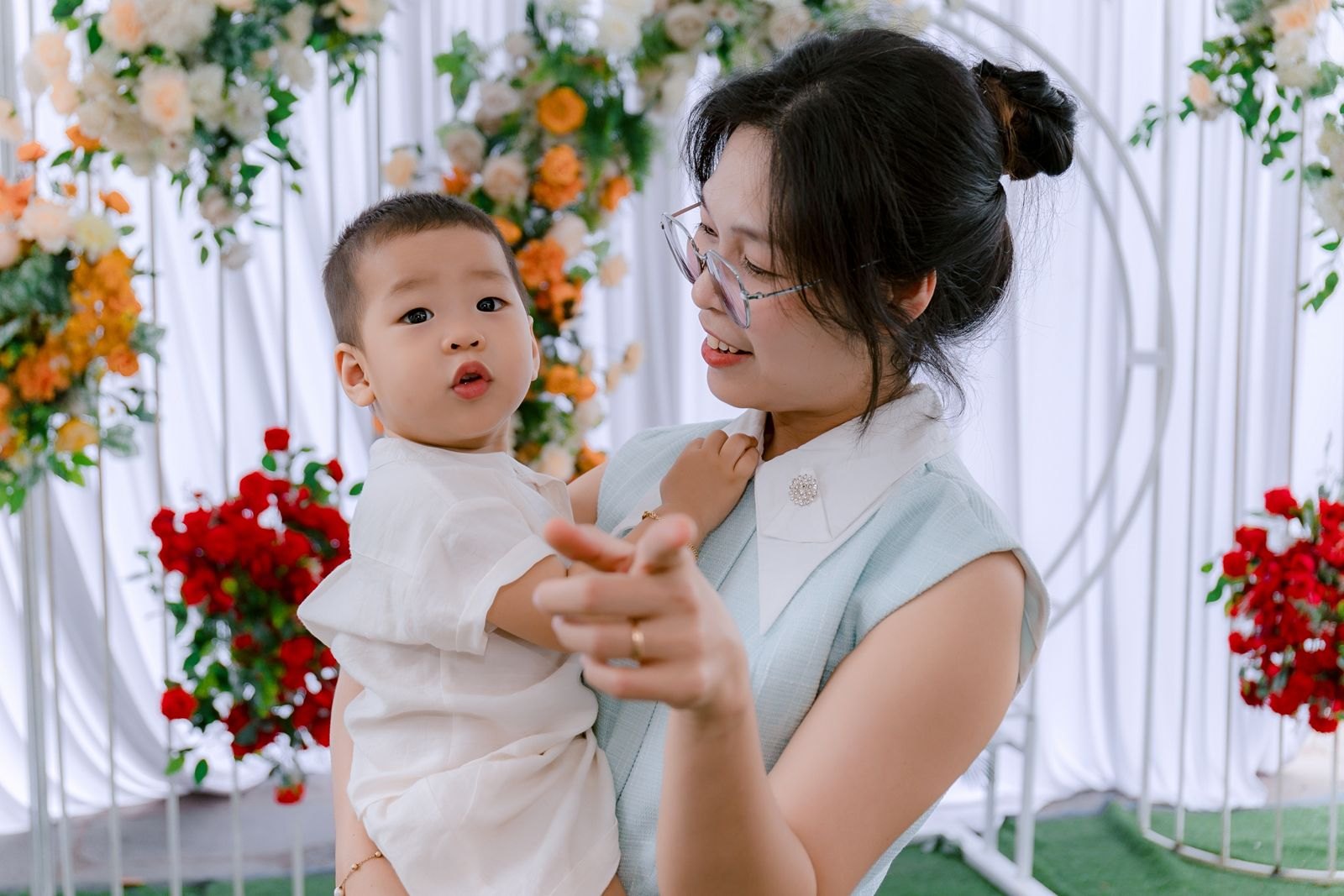 꽃으로 장식된 배경 앞에서 엄마가 아이를 안고 손을 마주 잡은 모습