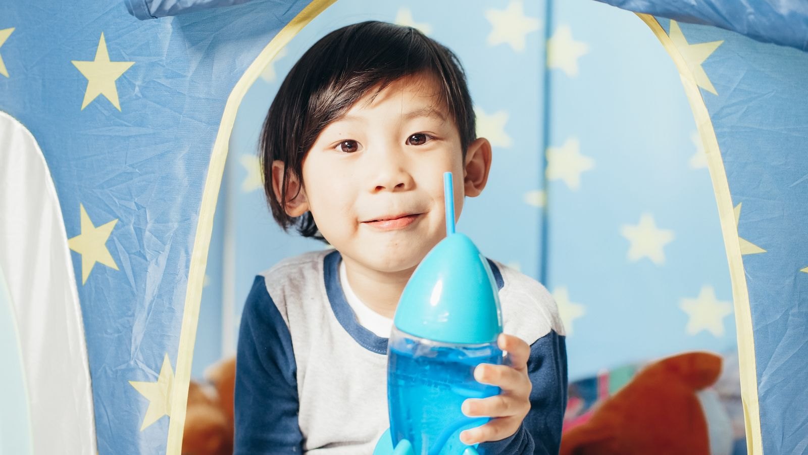 별무늬 놀이텐트 안에서 파란 빨대컵을 두 손으로 든 아이