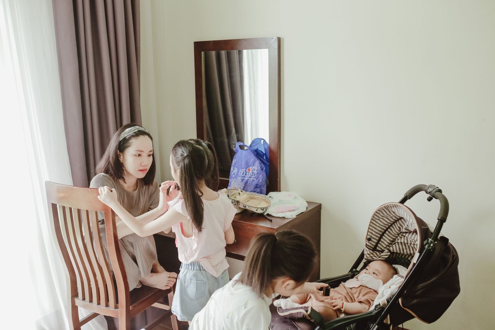 방 안에서 여성이 아이를 돌보는 옆에 아기가 탄 유모차가 놓여 있는 모습