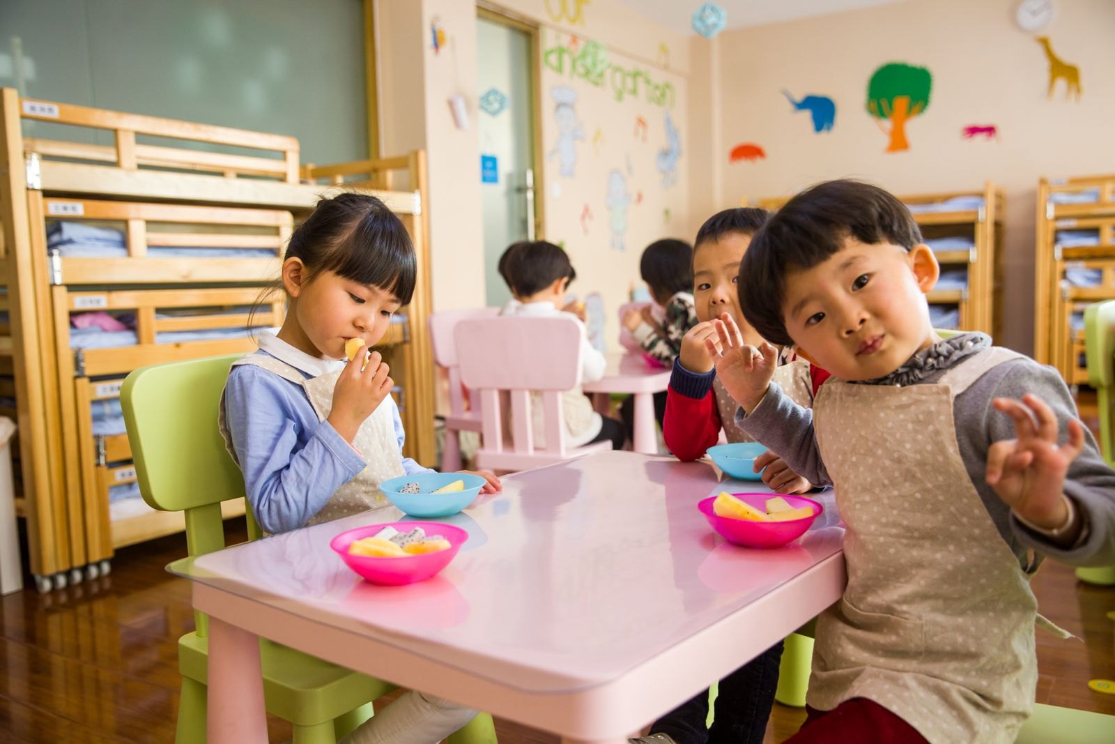 어린이집 교실에서 아이들이 분홍색 탁자에 둘러앉아 그릇을 앞에 둔 모습
