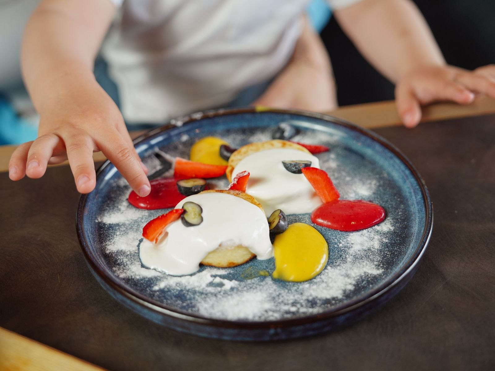 Kinderhandje dat voorzichtig naar een bord met onbekend eten reikt om het aan te raken voordat er iets wordt geproefd