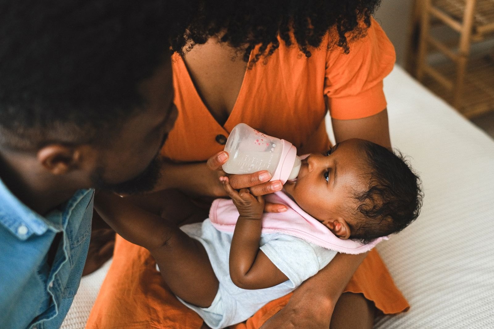 Een ouder geeft een baby de fles terwijl een ander gezinslid toekijkt